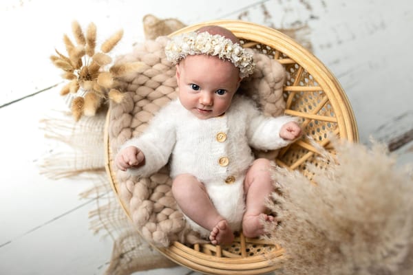 Baby in weißer Strickjacke sitzt in einem Rattankorb zwischen Pampasgras