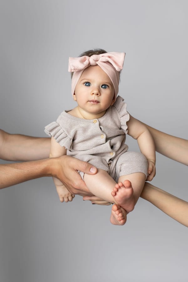 Elternhände halten ein Baby mit rosa Haarschleife vor grauem Hintergrund
