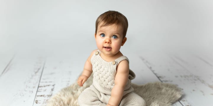Baby im Strickstrampler sitzt allein auf einem hellen Fell