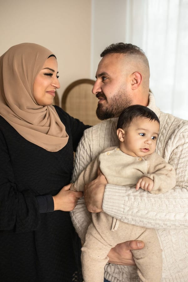 Eltern schauen sich an, Papa hält den kleinen Sohn im Strickpullover auf dem Arm