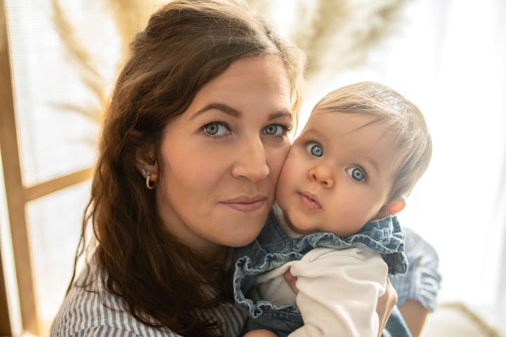 Mutter und Baby schmiegen Wange an Wange und schauen in die Kamera