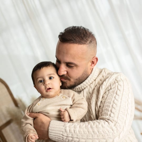 Papa küsst seinen kleinen Sohn auf die Wange, der Junge schaut in die Kamera