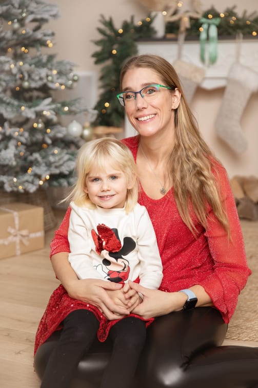 Mutter mit Brille hält ihre kleine Tochter auf dem Schoß, dahinter Tannenbaum und Strümpfe