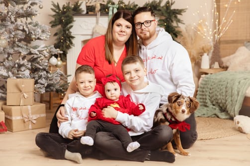 Eltern mit drei Kindern und ihrem Australian Shepherd vor dem Weihnachtsbaum