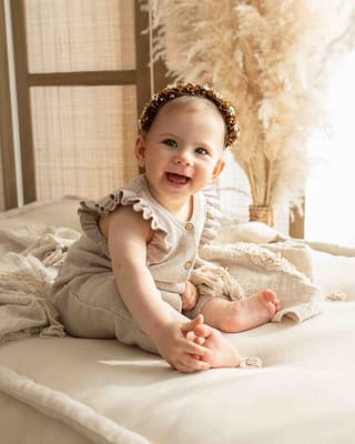 Sitzendes Baby mit Haarband lacht in die Kamera