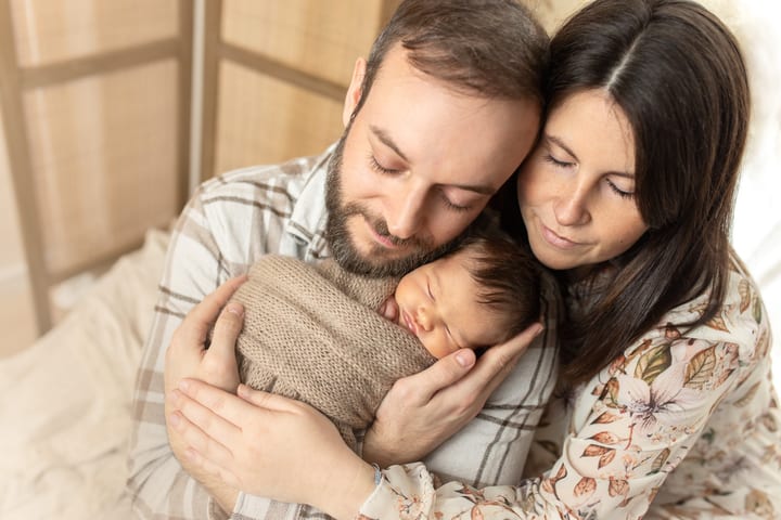 Eltern kuscheln mit ihrem schlafenden Neugeborenen im Arm