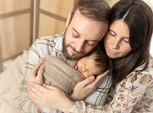 Eltern kuscheln mit ihrem schlafenden Neugeborenen im Arm